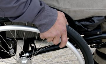 dłonie osoby niepełnosprawnej obracające koła wózka inwalidzkiego